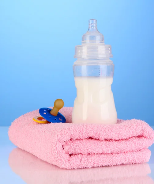 Bottle for milk with towels and nipple on blue background — Stock Photo, Image