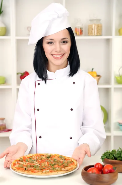 Hermosa chica jefe de cocina con pizza en el fondo de la cocina — Foto de Stock