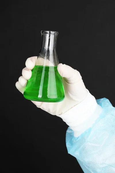Стеклянная трубка с жидкостью в руке ученого во время медицинских испытаний на черном фоне — стоковое фото