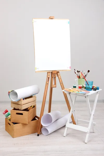 Wooden easel with clean paper and art supplies in room — Stock Photo, Image