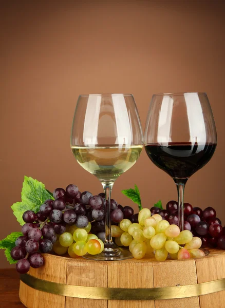 Glasses of red and white wine, grape on wooden barrel, on color background — Stock Photo, Image