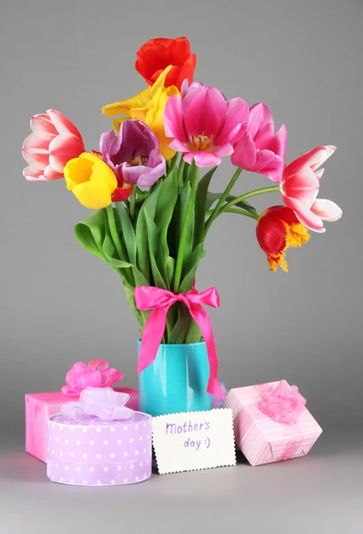 Schöne Tulpen im Strauß mit Geschenken und Notiz auf grauem Hintergrund — Stockfoto