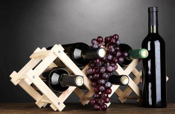 Bottles of wine placed on wooden stand on grey background — Stock Photo, Image