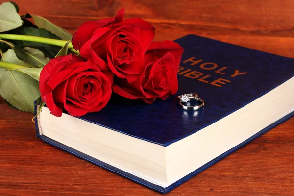 Wedding rings on bible with roses on wooden background