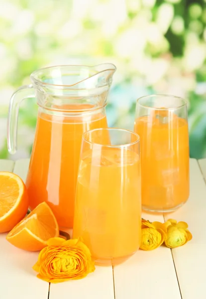 Glazen en werper sinaasappelsap op houten tafel, op groene achtergrond — Stockfoto