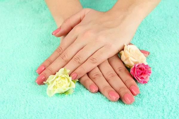 Mãos de mulher com manicure rosa e flores, em fundo de cor — Fotografia de Stock