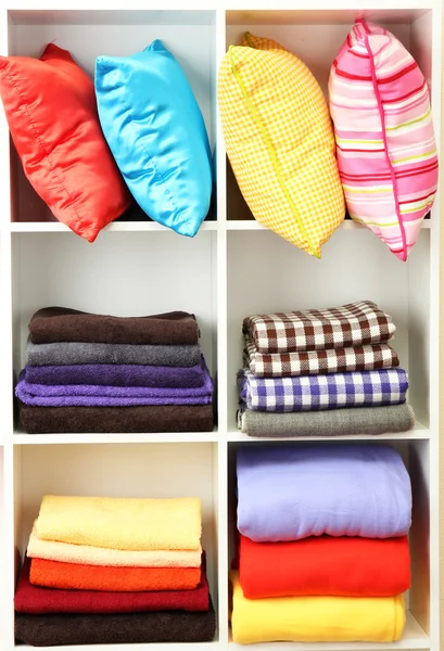 Bright pillows, towels and plaids on shelves, isolated on white — Stock Photo, Image