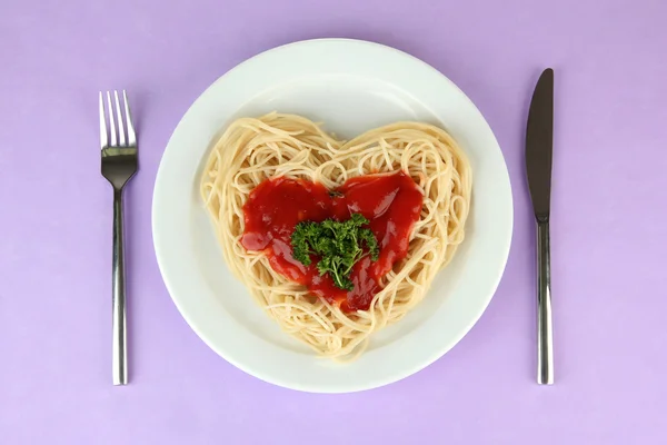 Cooked spaghetti carefully arranged in heart shape and topped with tomato sauce, on color background — Stock Photo, Image