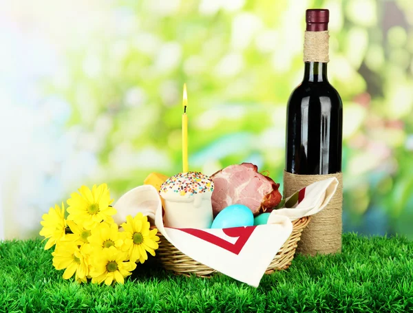 Easter basket: Conceptual photo of traditional easter food in wicker basket, on green grass, on bright background