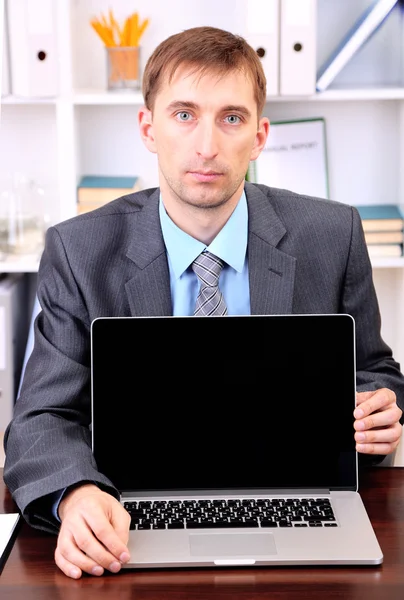Joven hombre de negocios con ordenador portátil frente a su lugar de trabajo — Foto de Stock