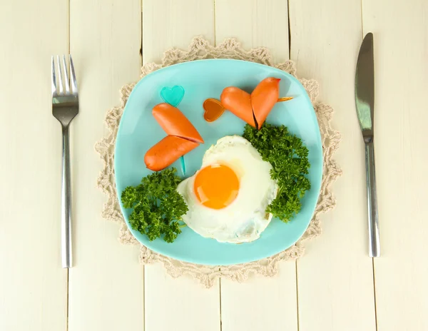 Sausages in form of hearts, scrambled eggs and parsley, on color plate, on wooden background — Stok fotoğraf