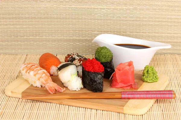 Delicioso sushi servido em tábua de madeira no tapete de bambu — Fotografia de Stock