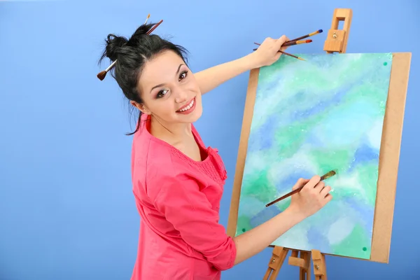 Schöne junge Malerin bei der Arbeit, auf farbigem Hintergrund — Stockfoto