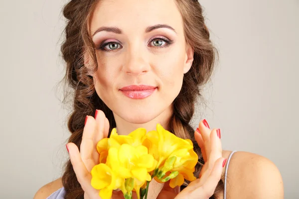 Giovane donna con bella acconciatura e fiori, su sfondo grigio — Foto Stock