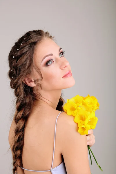 Mujer joven con hermoso peinado y flores, sobre fondo gris —  Fotos de Stock