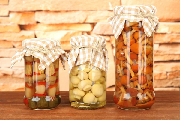 Delicious marinated mushrooms in glass jars, on wooden table on bright background — Stock Photo, Image