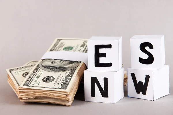 Cubos de papel branco rotulado "Notícias" com dinheiro em fundo cinza — Fotografia de Stock
