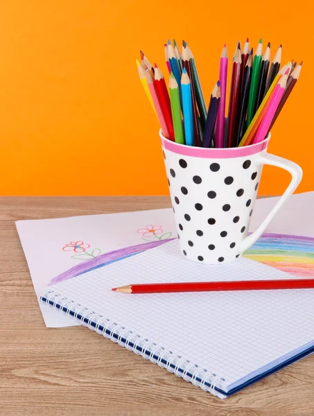 Färgglada pennor i cup på bordet på orange bakgrund — Stockfoto