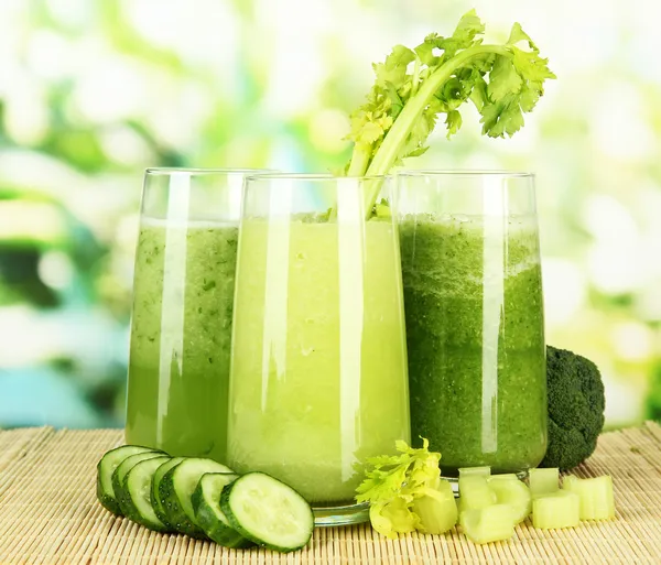 Bicchieri di succo di verdura verde su tappetino di bambù, su sfondo verde — Foto Stock