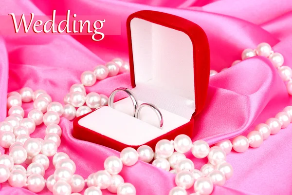 Anillos de boda en caja roja sobre fondo de tela rosa —  Fotos de Stock