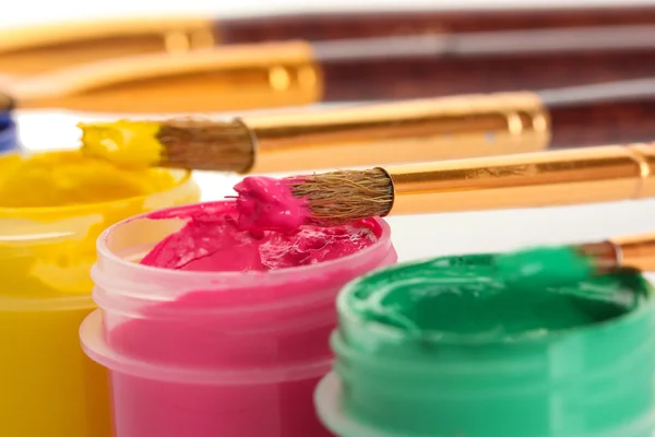 Brushes on the jars with colorful gouache on white background close-up — Stockfoto