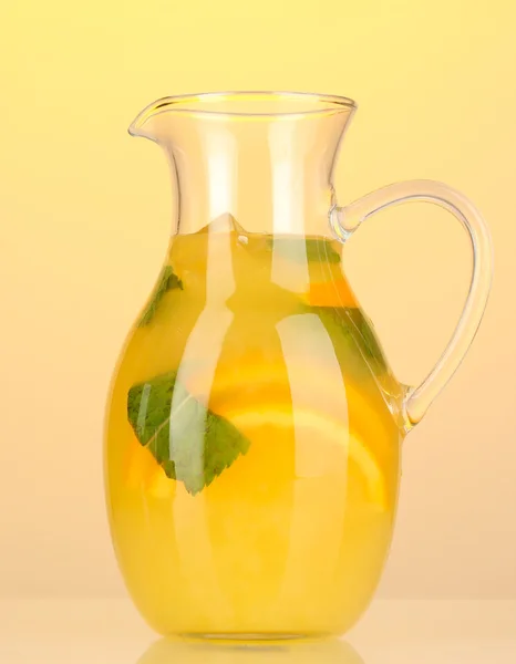 Orange lemonade in pitcher on yellow background — Stock Photo, Image