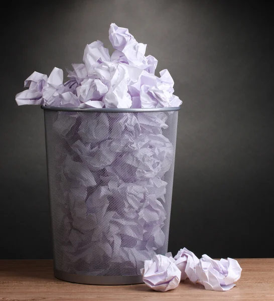 Metal trash bin from paper on wooden floor on gray background — Stock Photo, Image