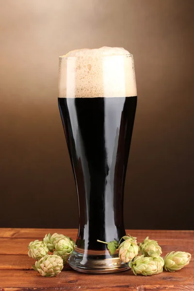 Μαύρη μπύρα σε ποτήρι και πράσινο λυκίσκο στο ξύλινο τραπέζι για καφέ φόντο — Φωτογραφία Αρχείου