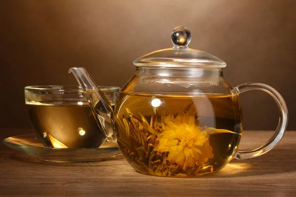 Tetera de vidrio y taza con té verde exótico sobre mesa de madera sobre fondo marrón — Foto de Stock