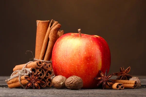 Bâtonnets de cannelle, pomme rouge, muscade et anis sur table en bois sur fond brun — Photo