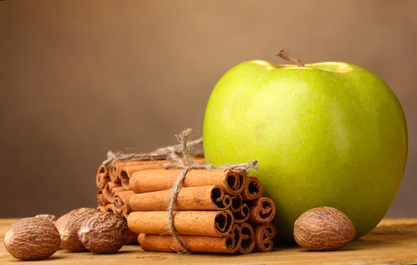 Bâtonnets de cannelle, pomme verte et muscade sur table en bois sur fond brun — Photo