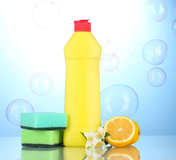 Folyékony mosogatószer, szivacsok és a citrom, a virágok, kék háttérrel — Stock Fotó