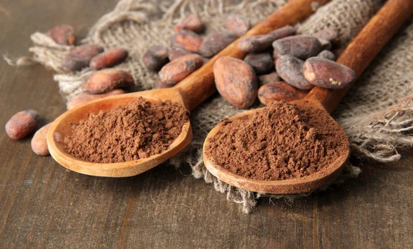 Poeder van de cacao in lepels en bonen op houten achtergrond — Stockfoto