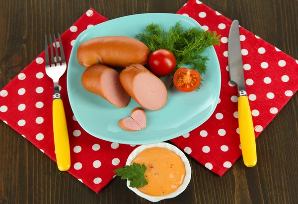 Sausage, greens, tomato on plate on wooden table — Stock Photo, Image