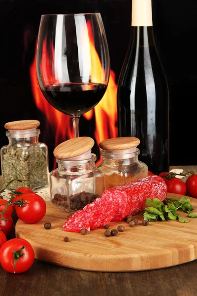 Smakelijke salami aan boord van houten tafel op brand achtergrond — Stockfoto