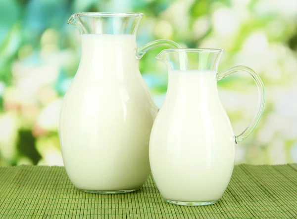 Brocche di latte sul tavolo su sfondo luminoso — Foto Stock