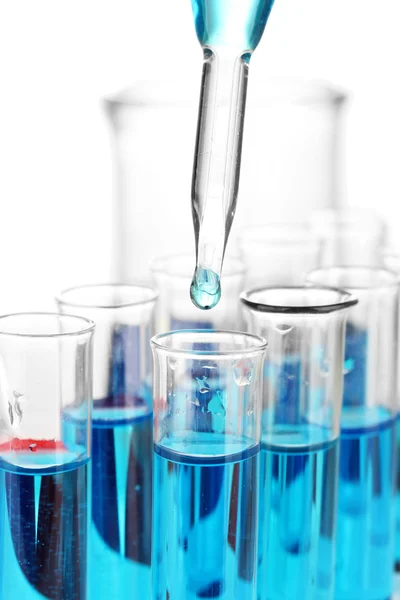 Pipette de laboratoire avec goutte de liquide de couleur sur éprouvettes en verre, en gros plan, isolée sur blanc — Photo