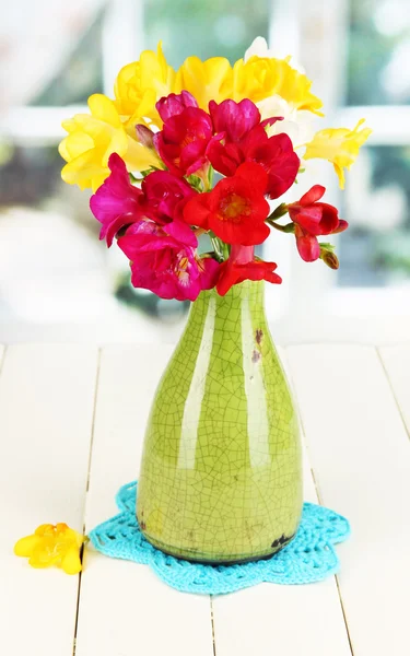 Beautiful bouquet of freesia in blue vase on wooden table on window background — Stock Photo, Image