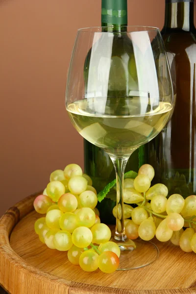 Composition of wine bottles, glass of white wine, grape on wooden barrel, on color background — Stock Photo, Image