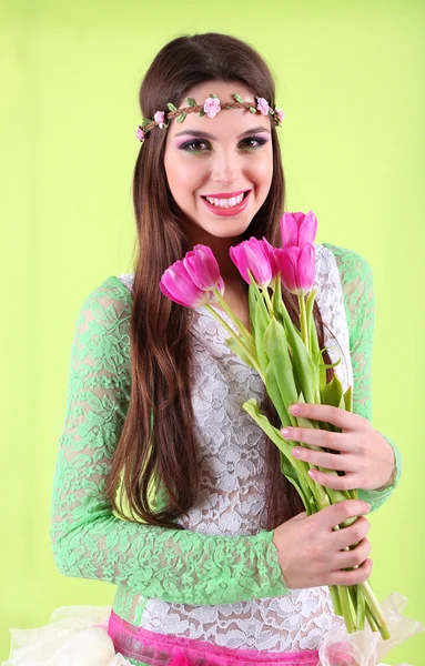 緑色の背景で、花の花束を保持している彼女の頭の上の輪飾りを持つ美しい少女 — ストック写真