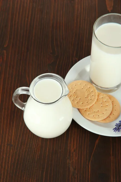 Un vaso de leche, una jarra y galletas sobre un fondo de madera — Foto de Stock