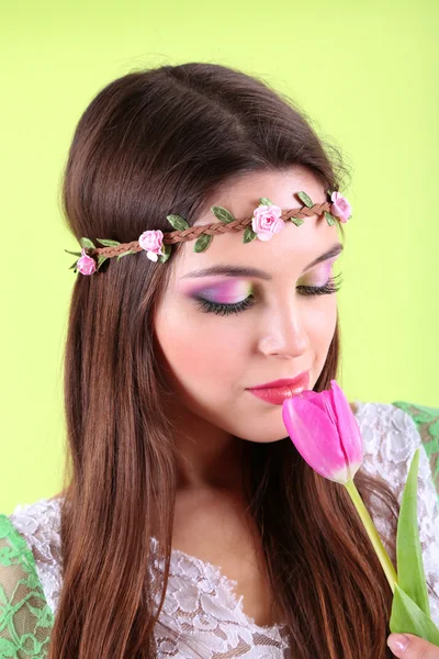 Young beautiful girl in decorative wreath with tulip in her hand, on green background Stock Image