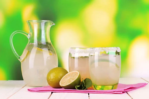 Limonata di agrumi in brocca e bicchieri su tavolo in legno su sfondo naturale — Foto Stock