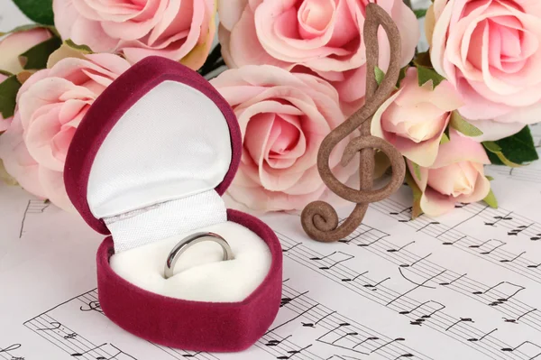 Chiave di violino, rose e scatola con anello nuziale su sfondo musicale — Foto Stock