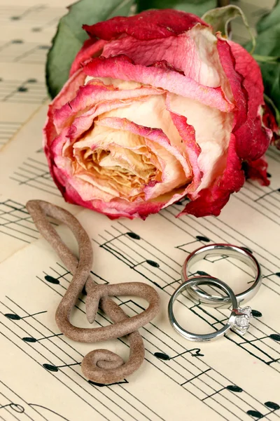 Treble clef, rose en trouwringen op muzikale achtergrond — Stockfoto