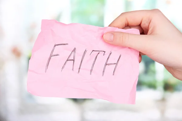 Слово веры на листе бумаги в руке на фоне окна — стоковое фото