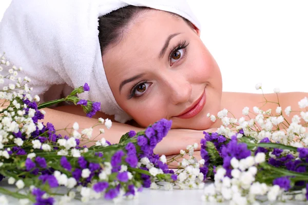 Mooie jonge vrouw met handdoek op haar hoofd en bloemen geïsoleerd op wit — Stockfoto