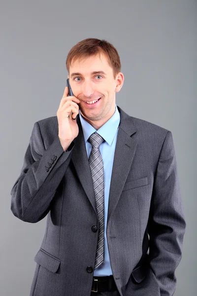 Jovem empresário falando por telefone celular em fundo cinza — Fotografia de Stock