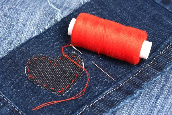 Heart-shaped patch on jeans wiht needle and thread closeup — Stock Photo, Image