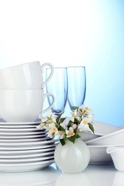Empty clean plates, glasses and cups with dishwashing liquid and flowers on blue background — Stock Photo, Image